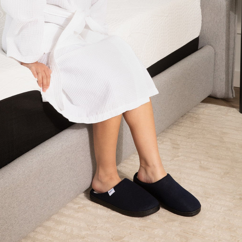 Woman in a white robe and black slippers sitting on a gray couch.